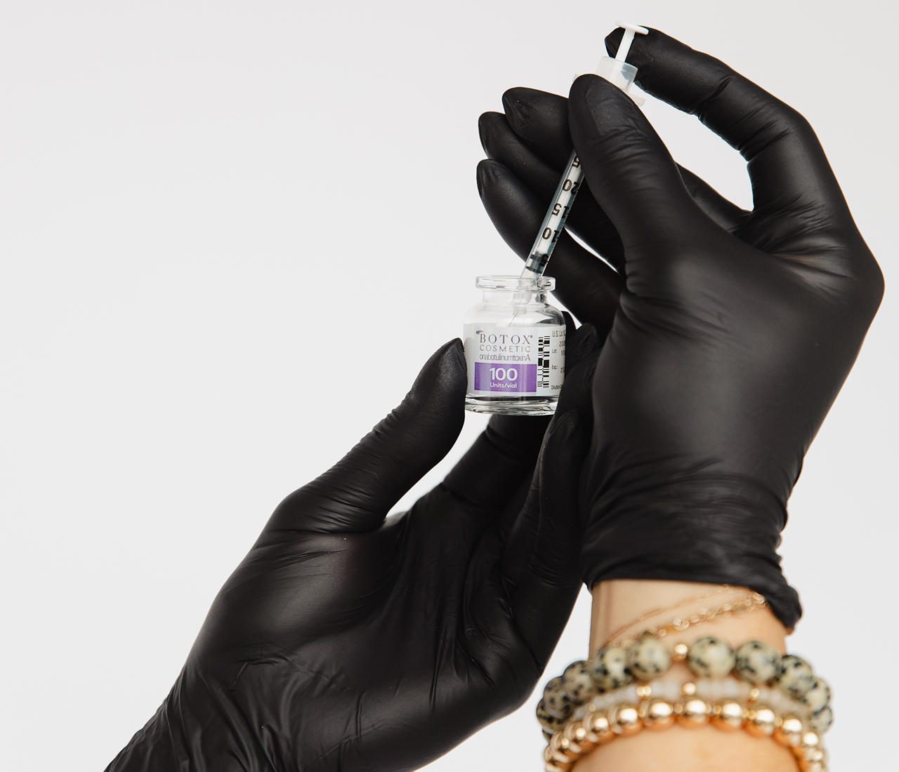 Gloved hands holding a small vial of COVID-19 vaccine.