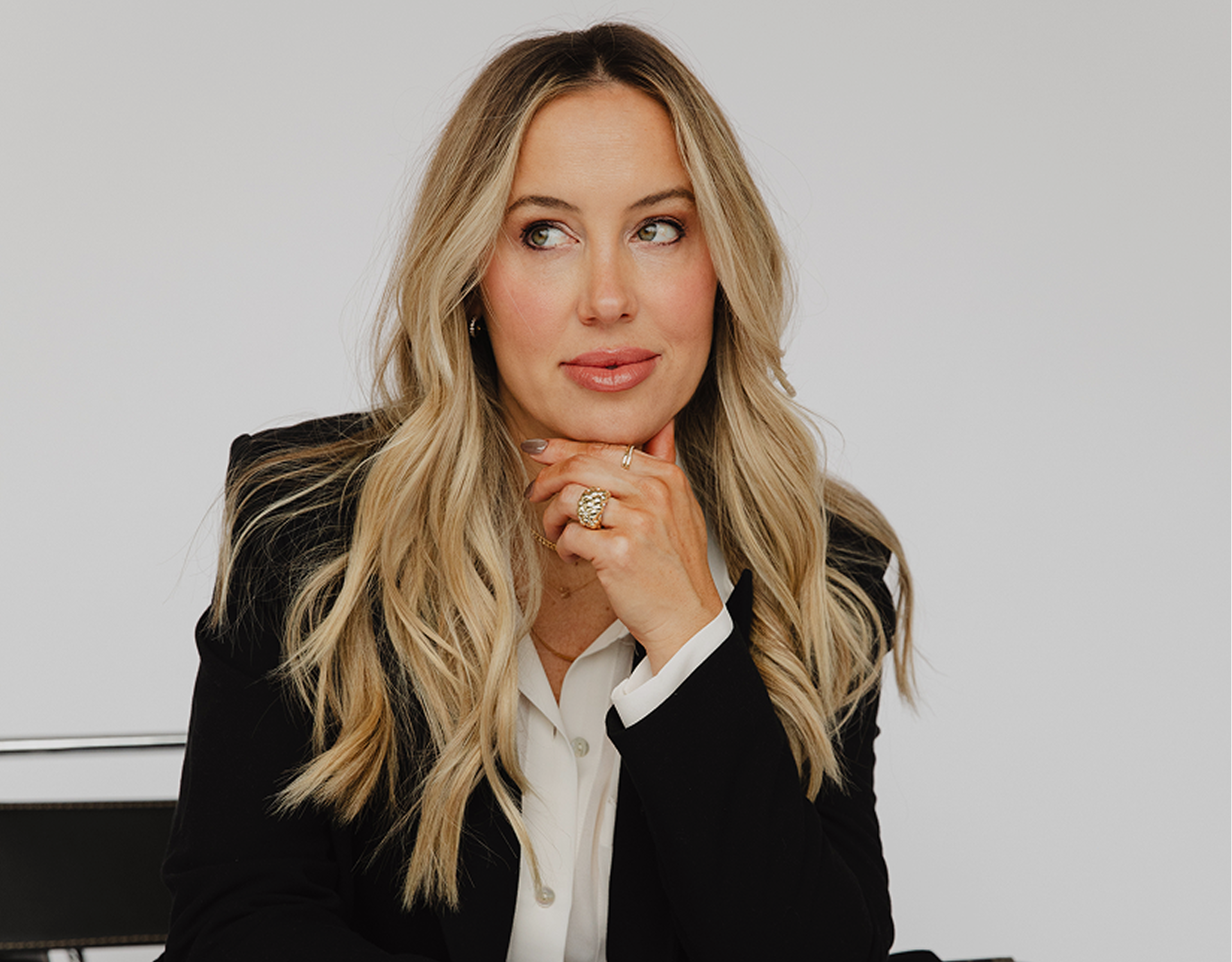 Blonde woman in black blazer thoughtfully looking to the side.